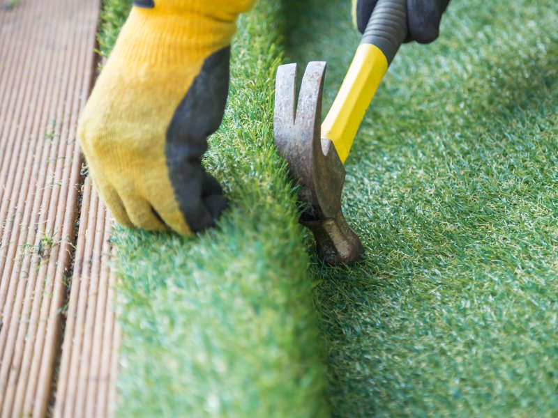 professional with yellow gloves and hammer installing artificial grass