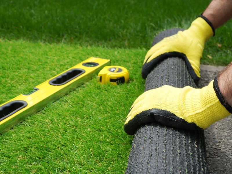 professional with yellow gloves rolling out artificial grass