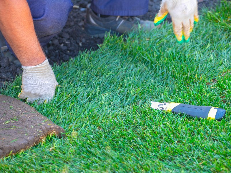 professional with gray gloves installing artificial grass with tool